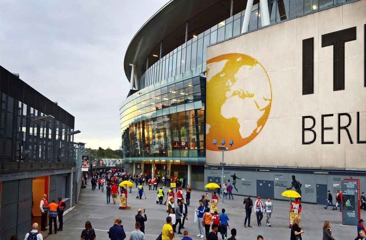 The bustling venue of ITB Berlin 2025, featuring attendees, yellow umbrella stands, and a large billboard displaying 'ITB BERLIN' with a globe graphic. This setting symbolizes the collaboration between Regenera Luxury, UNWTO, the World Sustainable Hospitality Alliance, and ITB Berlin to champion gender equality, sustainability, and regenerative tourism through the International Awards of Equality in Tourism.
