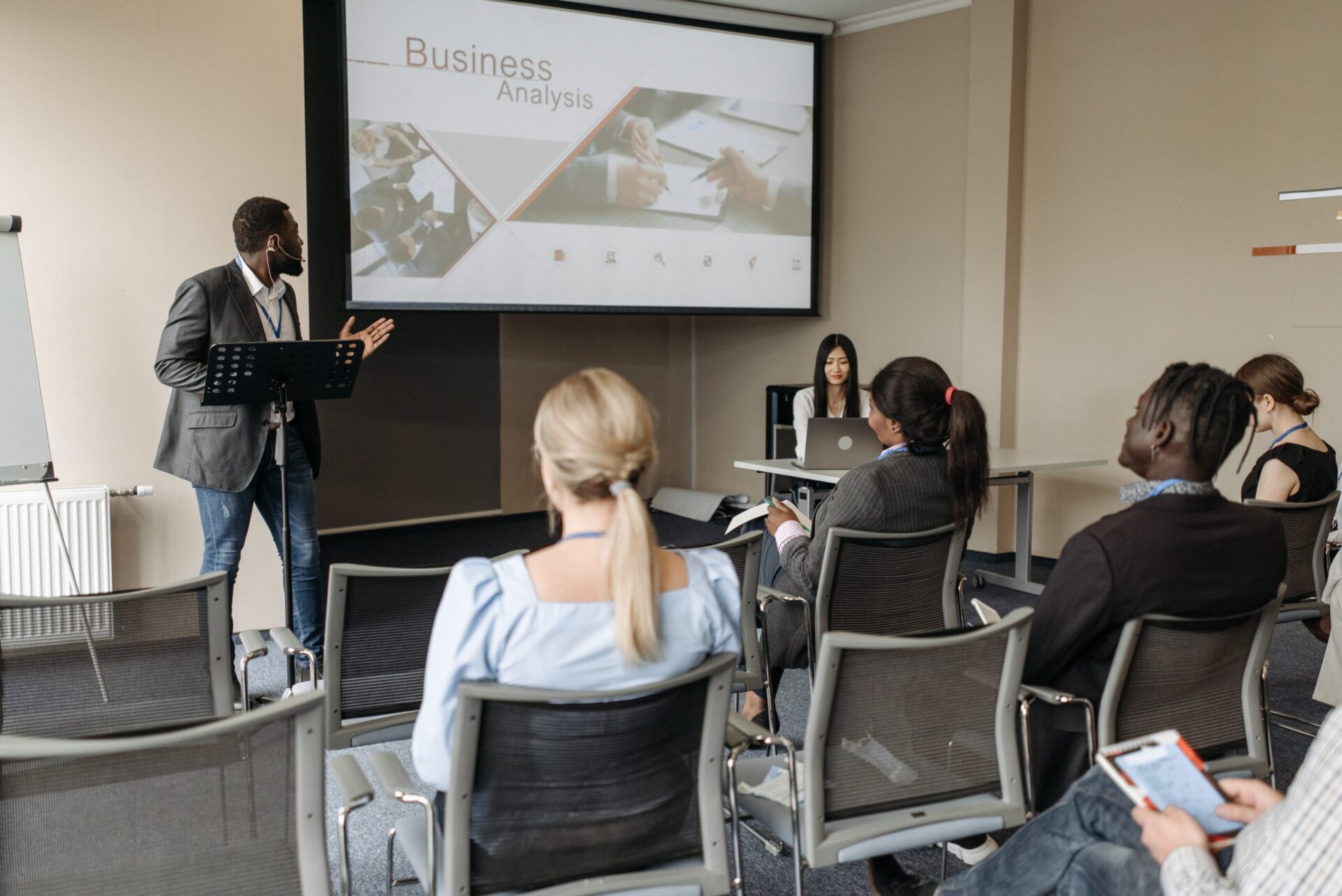 A group of young individuals actively participating in a workshop or training session at a boutique hotel setting. The setting includes a presenter engaging with the audience, showcasing a collaborative learning environment. This reflects the Young Talent Internship Program's mission to equip future industry leaders with knowledge in hotel operations, sustainability practices, and marketing, while fostering a commitment to regenerative sustainability.