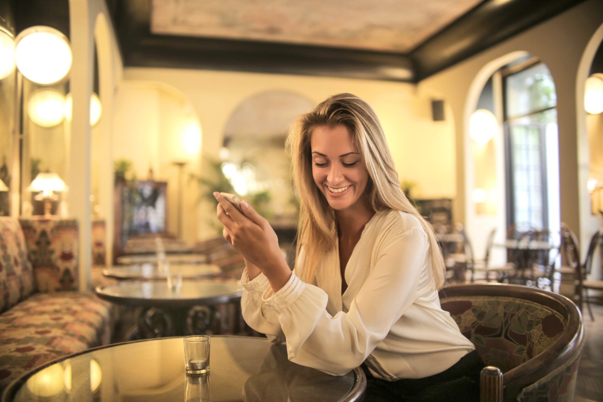 An elegant café or boutique hotel setting with large windows, stylish furniture, and a person using a smartphone at a table. The image symbolizes connection and engagement, aligning with the REGENERA association's mission to promote sustainability, ethical luxury, and positive impact in the boutique hotel industry through global initiatives and education