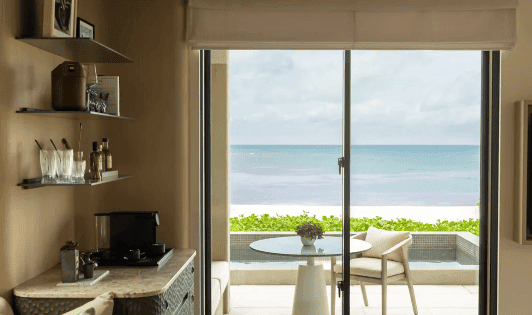 'A tranquil resort room with ocean views in Miyakojima, showcasing Rosewood’s commitment to 'A Sense of Place.' The space integrates natural materials like Ryukyu limestone and reclaimed wood, reflecting the serene Ryukyu Islands and promoting Regenera Luxury values of sustainability and community enrichment.'