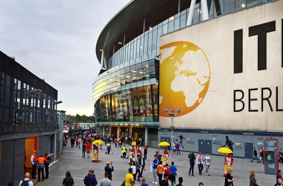 The bustling venue of ITB Berlin 2025, featuring attendees, yellow umbrella stands, and a large billboard displaying 'ITB BERLIN' with a globe graphic. This setting symbolizes the collaboration between Regenera Luxury, UNWTO, the World Sustainable Hospitality Alliance, and ITB Berlin to champion gender equality, sustainability, and regenerative tourism through the International Awards of Equality in Tourism.