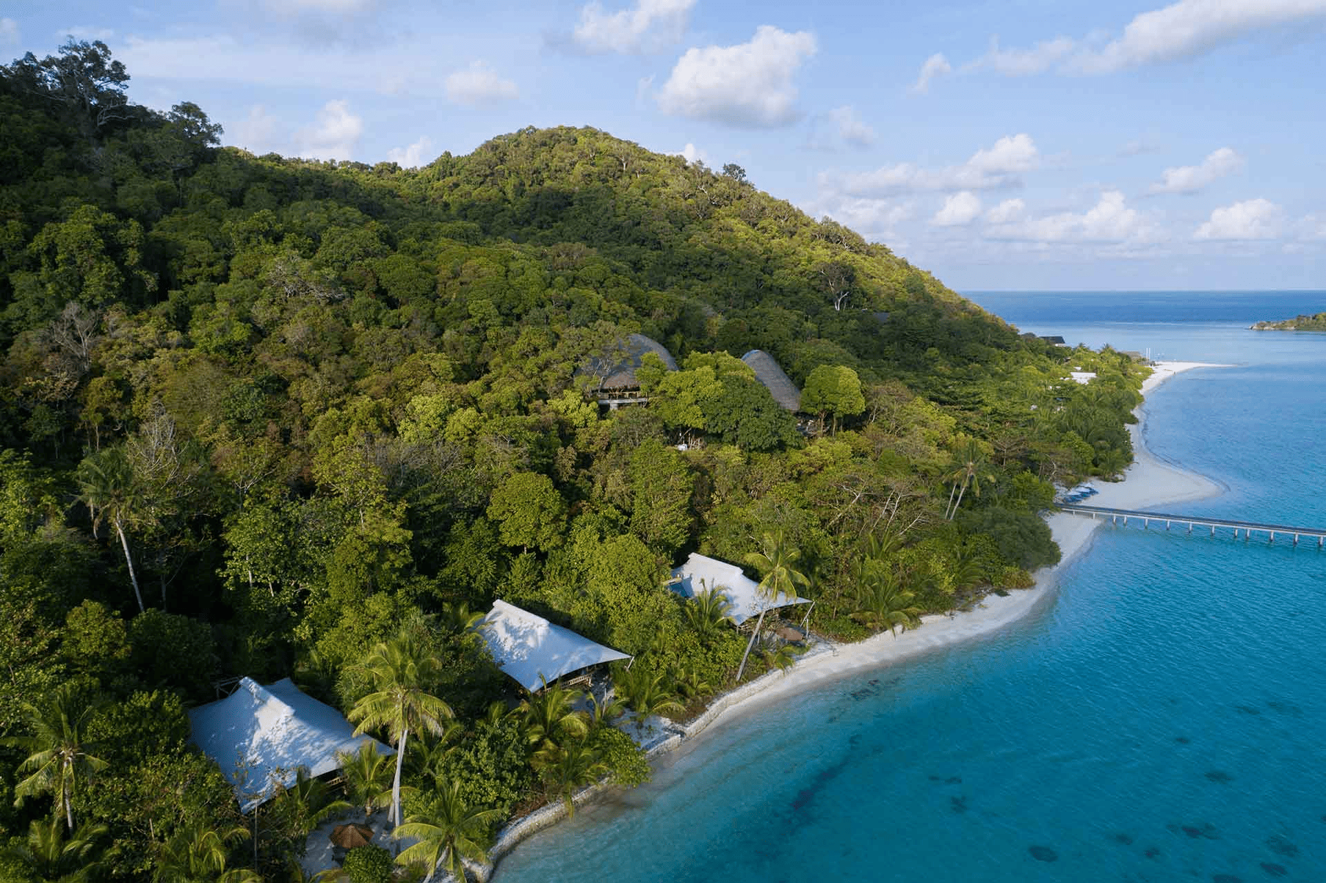 a oceanic view of Bawah Reserve An eco-resort in the Anambas Islands, Indonesia. the island is surrounded by tropical trees and the the tent like houses surrounded by coconut tree.